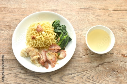 dry Chinese egg yellow noodles with red barbecue pork and dumpling in on plate with clear soup cup photo