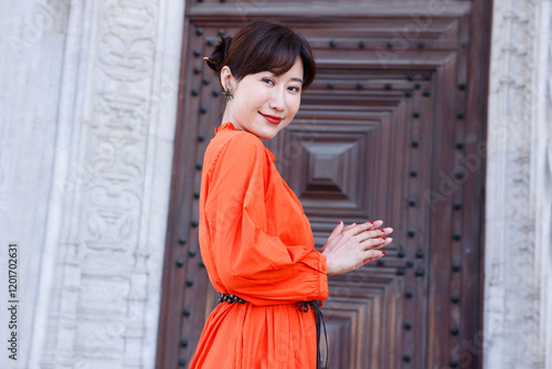 A young beautiful asian woman stands in front of beautiful architecture in Lisbon, Portugal. She pushes her hair back out of her face in a spontaneous, candid, real moment. She smiles at the camera.