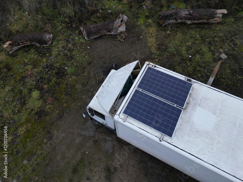 the traveler has a solar panel on the roof racks on the roof of small camper van. Very simply, he can use the sun to charge the batteries and light the inside of car, home made, meadow, white, stove photo