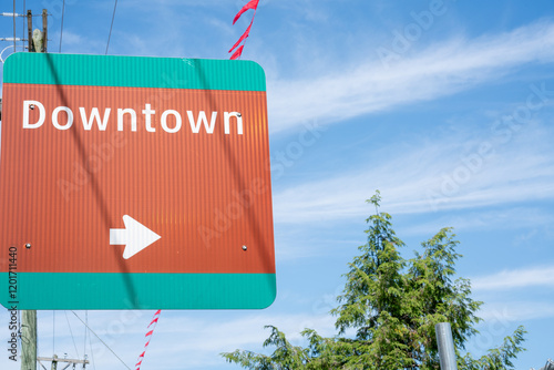 A directional sign indicating downtown with an arrow, set against a clear blue sky and lush green trees