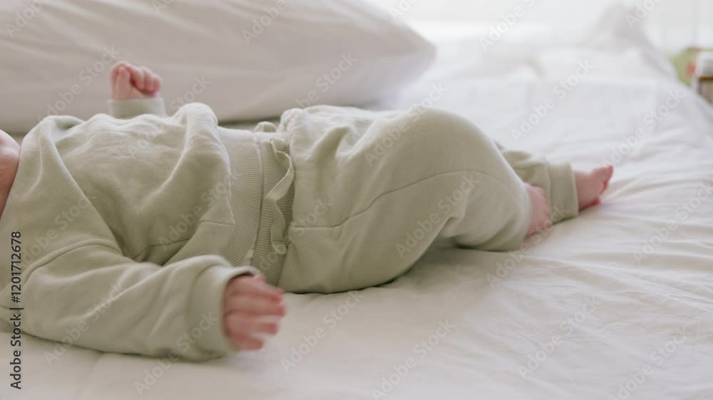Baby lying on bed on back actively moving legs and arms. Small child in green khaki suit relaxed on back playing with hands and arms. Healthy developed child Baby lying on bed on back actively moving legs and arms. Small child in green khaki suit relaxed on back playing with hands and arms. Healthy developed child