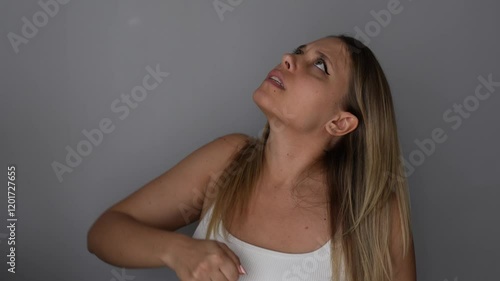 A young furious caucasian blonde woman swearing at the upstairs neighbours shaking her fist on dark grey background. The girl unhappy with the noise looks up. Loud music or sound from renovation