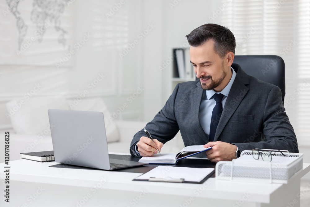 Handsome banker making notes at table in office Handsome banker making notes at table in office