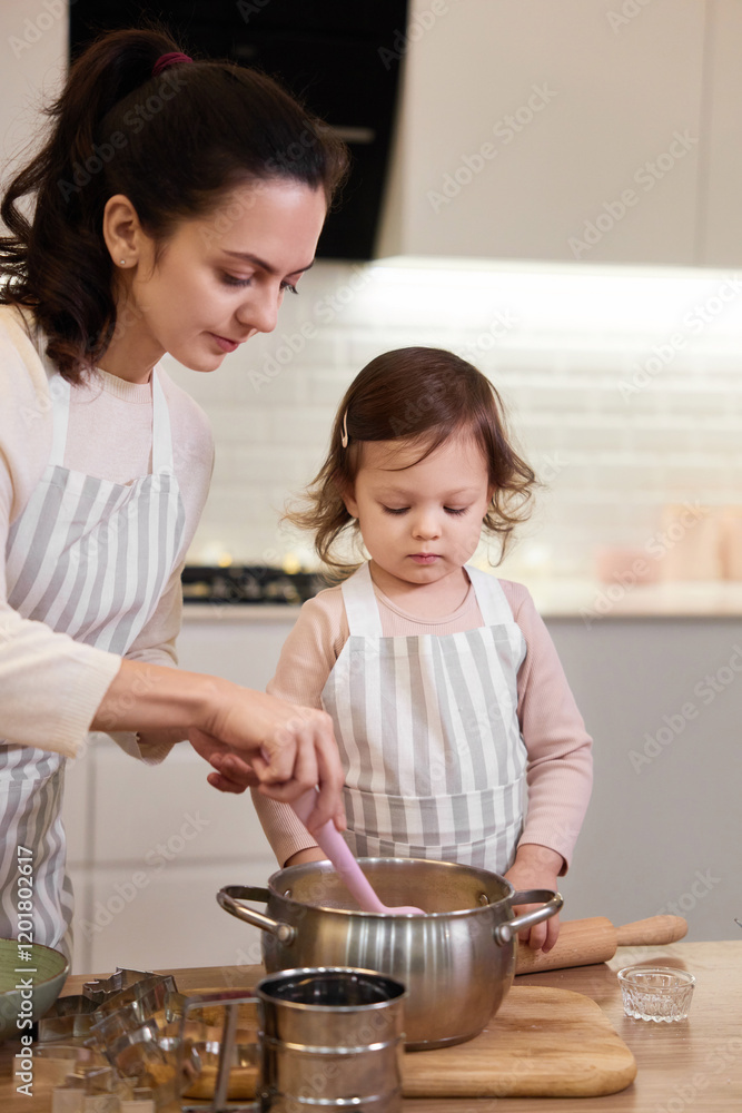 mother and her little child daughter in aprons preparing the dough in the kitchen, bake cookies mother and her little child daughter in aprons preparing the dough in the kitchen, bake cookies
