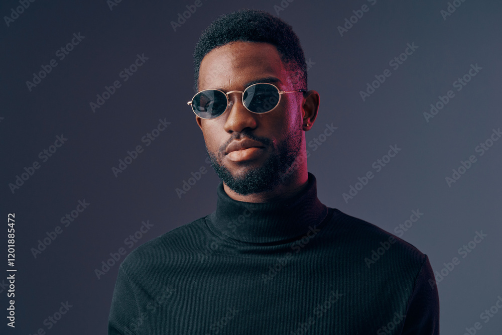 Fototapeta premium Stylish young man with sunglasses in a turtleneck sweater, expressing confidence against a dark gradient background, ideal for fashion and lifestyle themes