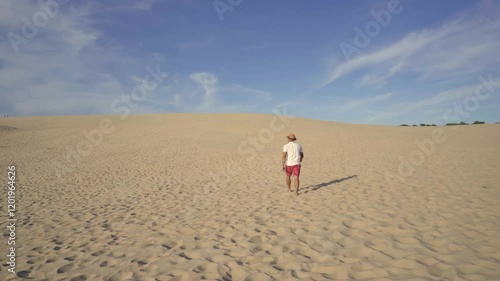 young man walking on large sand dune in pilat arcachon france and throwing hat in the air