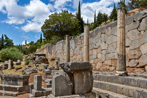 Ancient ruins of the Temple of Apollo in Delphi, Greece, showcasing preserved stone columns and a polygonal wall with a scenic mountainous backdrop.