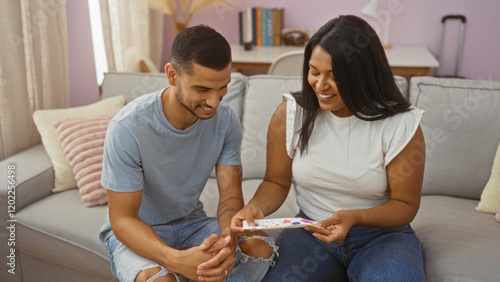 Fotografi Couple sitting on a couch, smiling and sharing a moment while holding a colorful