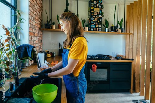 Side view of nice looking woman gardener wearing black gloves washing rinses the cactus root from the soil in kitchen. photo