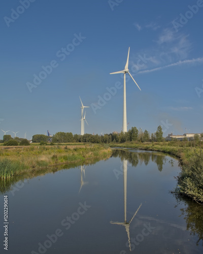 Nature reserve of Rieme in the harbor of Ghent, with wind turbines reflecting in a creek, and industrial building in the distance. Flanders, Belgium  photo