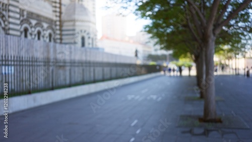 Blurred image of marseilles street outdoors with bokeh effect, trees lining the pathway and defocused buildings in the background under clear skies.