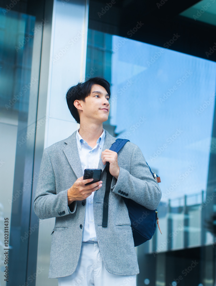 A smiling Successful Confident Asian businessman using smartphone to browse the internet, typing message standing outdoors office building. Confident asian male worker using mobile phone outdoors. A smiling Successful Confident Asian businessman using smartphone to browse the internet, typing message standing outdoors office building. Confident asian male worker using mobile phone outdoors.