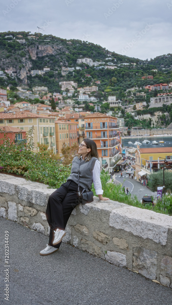 Obraz premium Woman smiling in villefranche france with scenic european seaside view showcasing colorful architecture and vibrant hillside.