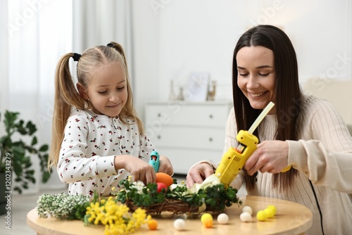 Mother and daughter with hot glue guns creating Easter composition at table indoors photo