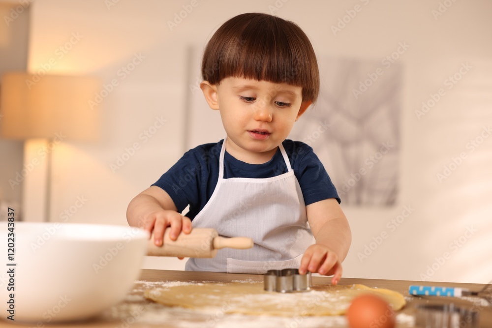 Cute little boy with rolling pin and cookie cutter at table indoors Cute little boy with rolling pin and cookie cutter at table indoors