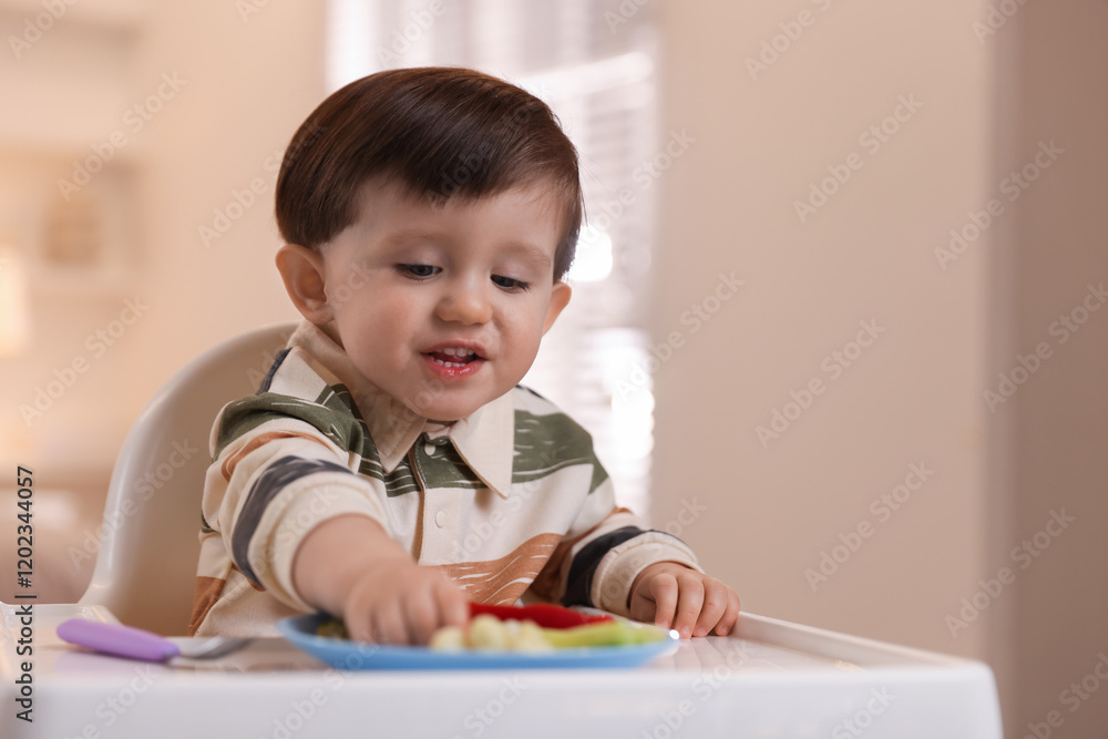 Cute little baby eating healthy food in high chair at home Cute little baby eating healthy food in high chair at home