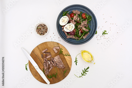 A fresh salad with tender beef, nutritious eggs, and fresh greens aragula, olive oil, seeds perfect for healthy meals anytime. Cutting ingredients on cutboard. photo