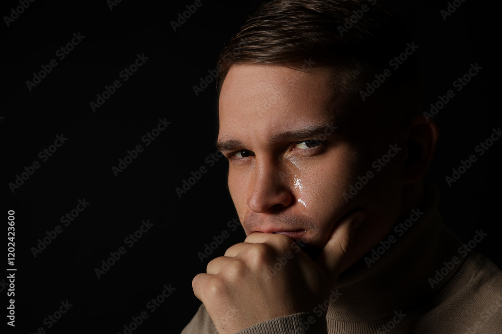 Distressed young man crying on black background. Space for text