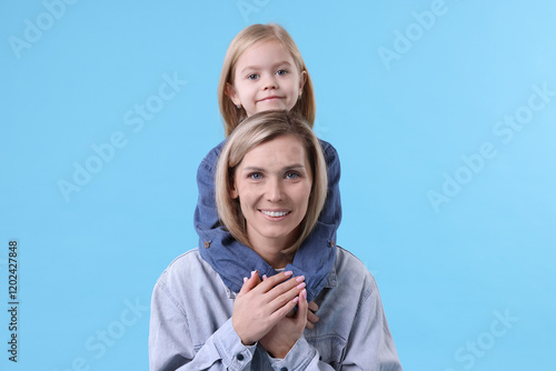 Cute little girl hugging her mom on light blue background. Happy Mother's Day photo