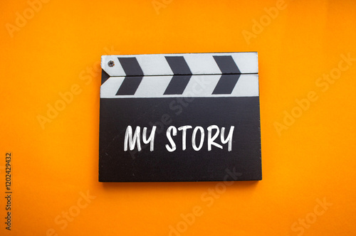 Fotografie My story message written on movie clapper board with orange background