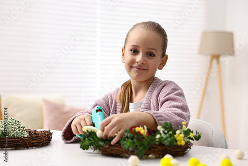 Little girl with hot glue gun creating Easter composition at table indoors photo