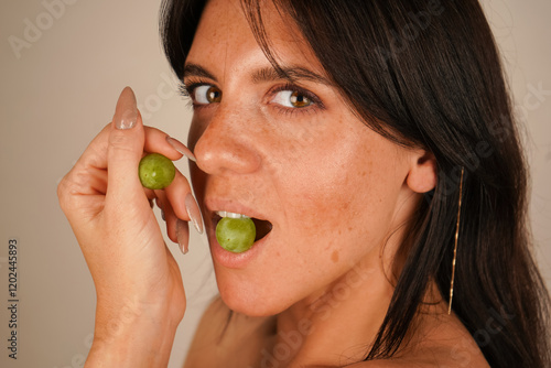 Beautiful young brunette woman with grapes, indoors. Portrait of beautiful girl hand holding fresh bunch of grapes, close-up. photo