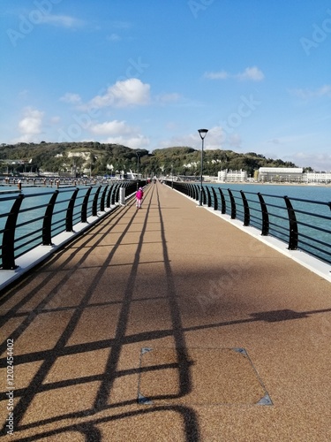 Long pier stretches out over tranquil water under a clear blue sky near coastal hills