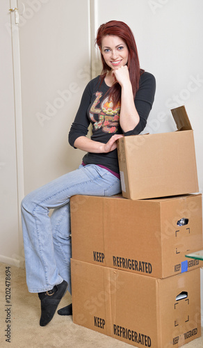 Cute young red-haired woman sitting on cardboard moving boxes having just moved into home or apartment photo