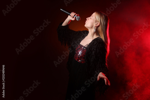 Beautiful singer performing on dark background with red light and smoke photo