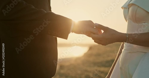 Wedding couple holding hands on sunset background. Close up. Beautiful bride and groom near the ocean.Honeymoon romantic couple in love walking in nature. Lovers or newlywed married by the sea.