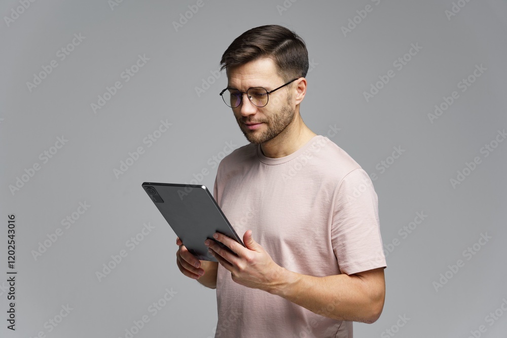 Man using a tablet while standing against a neutral gray background in a modern indoor setting Man using a tablet while standing against a neutral gray background in a modern indoor setting
