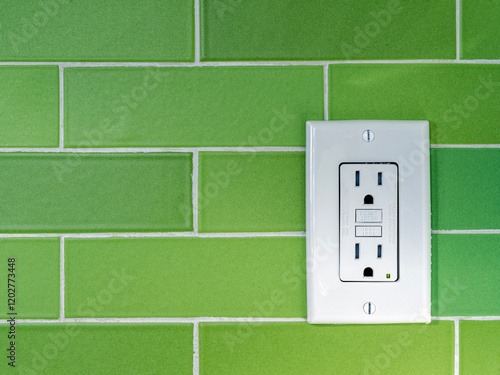 A GFCI (Ground Fault Circuit Interrupter) electrical outlet on a green tiled wall