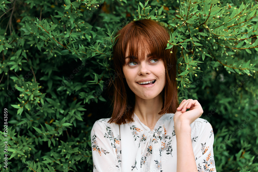 Confident redhead woman posing in front of lush green bushes with hands on hips Confident redhead woman posing in front of lush green bushes with hands on hips