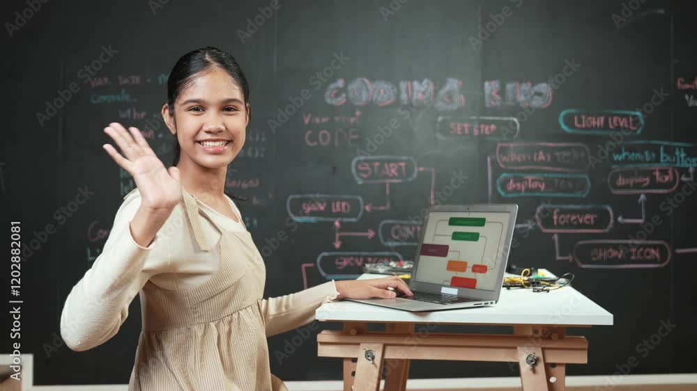 Smart high school girl waving to camera while programming code at blackboard with engineering code or prompt written. Academic student working on laptop or writing program and greeting. Edification Smart high school girl waving to camera while programming code at blackboard with engineering code or prompt written. Academic student working on laptop or writing program and greeting. Edification