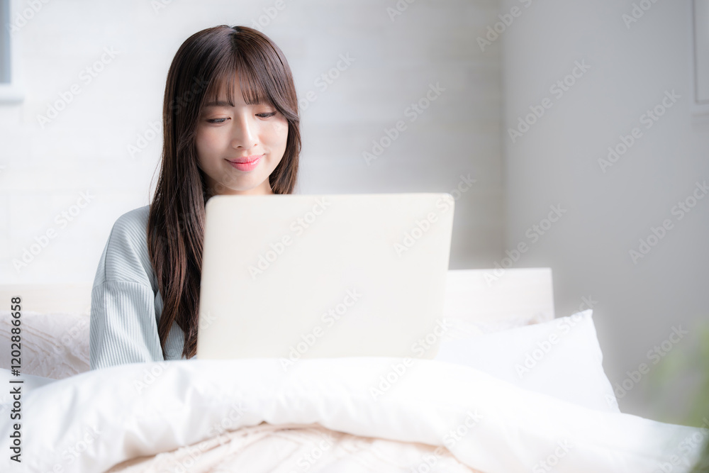 ベッドの上でパソコンをする俯く女性 ライフスタイルやフリーランス、働き方や忙しい仕事のイメージ ベッドの上でパソコンをする俯く女性 ライフスタイルやフリーランス、働き方や忙しい仕事のイメージ
