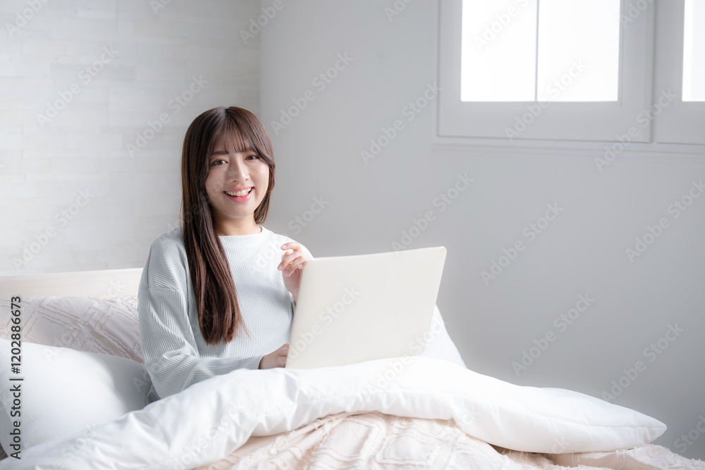 ベッドの上でパソコンをする女性 ライフスタイルやフリーランス、働き方や忙しい仕事のイメージのカメラ目線 ベッドの上でパソコンをする女性 ライフスタイルやフリーランス、働き方や忙しい仕事のイメージのカメラ目線