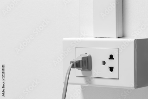 Plug from an electrical appliance. plugged into an electrical outlet on white wall background.
