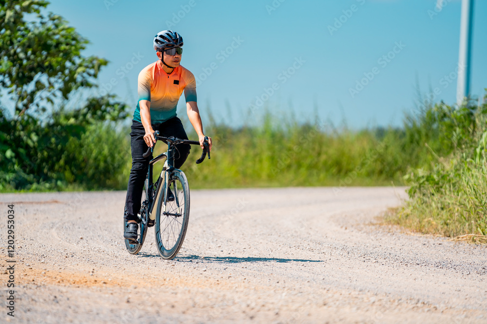 Fototapeta premium Bicyclist riding along a gravel path under a clear blue sky in warm weather