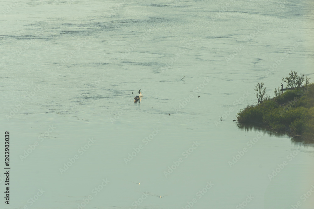 Landscape of fisherman in a boat on a river and layer mountains background.Fishermans in boat on a mountain lake at dawn, fog and forested shores. Landscape of fisherman in a boat on a river and layer mountains background.Fishermans in boat on a mountain lake at dawn, fog and forested shores.