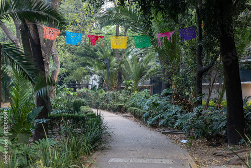 A banner of brightly colored papel picado (perforated paper) flutters above the tree-lined pedestrian median of the streets of the trendy La Condesa neighborhood in Cuauhtemoc borough in Mexico City.