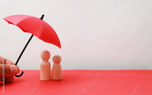 Couple of wooden figures of a man and a woman covered by an red umbrella. the concept of husband and wife protection