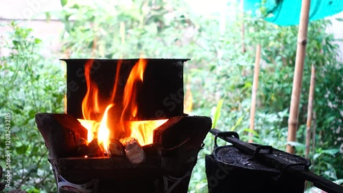 In a simple and old-fashioned way, cooking food with a stainless steel pot and an Anglo charcoal stove. to get a dark sooty color over a long time. The charcoal stove has a red light on it.