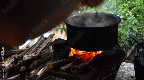 In a simple and old-fashioned way, cooking food with a stainless steel pot and an Anglo charcoal stove. to get a dark sooty color over a long time. The charcoal stove has a red light on it.