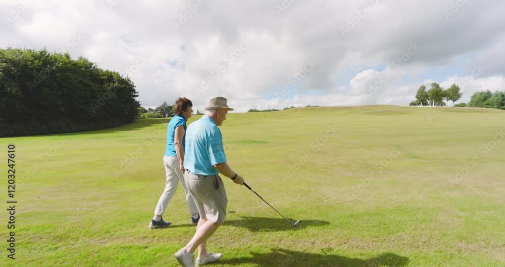 Male and female golf players wearing uniforms, talking and walking with clubs on golf course Male and female golf players wearing uniforms, talking and walking with clubs on golf course