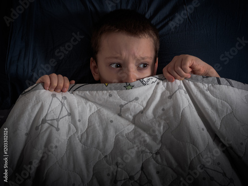 The boy hides under the covers in bed, trying to get rid of the nightmares and find solace in the dark. photo