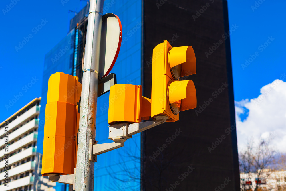 Modern city street scene with yellow traffic lights against a blue glass building and bright sky. Urban architecture, transportation infrastructure, and contemporary city life depicted