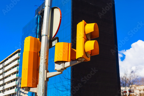 Obraz na płótnie Modern city street scene with yellow traffic lights against a blue glass building and bright sky. Urban architecture, transportation infrastructure, and contemporary city life depicted w salonie