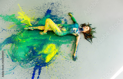 sexy redheaded woman elegant on the floor in blue, green, yellow color, abstractly painted woman on the splashed ground, abstract body art painting.