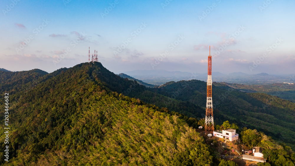 Obraz premium A panoramic aerial view of a telecommunications tower standing tall on a lush green mountaintop against a clear blue sky.