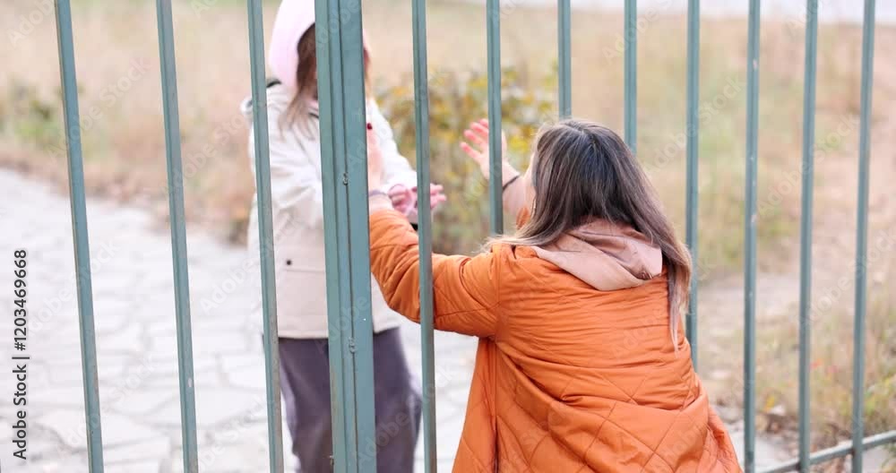 Mother greets smiling daughter with loving embrace. Cheerful mother waits for kid behind fence and extends hands to hug daughter. Slow motion Mother greets smiling daughter with loving embrace. Cheerful mother waits for kid behind fence and extends hands to hug daughter. Slow motion